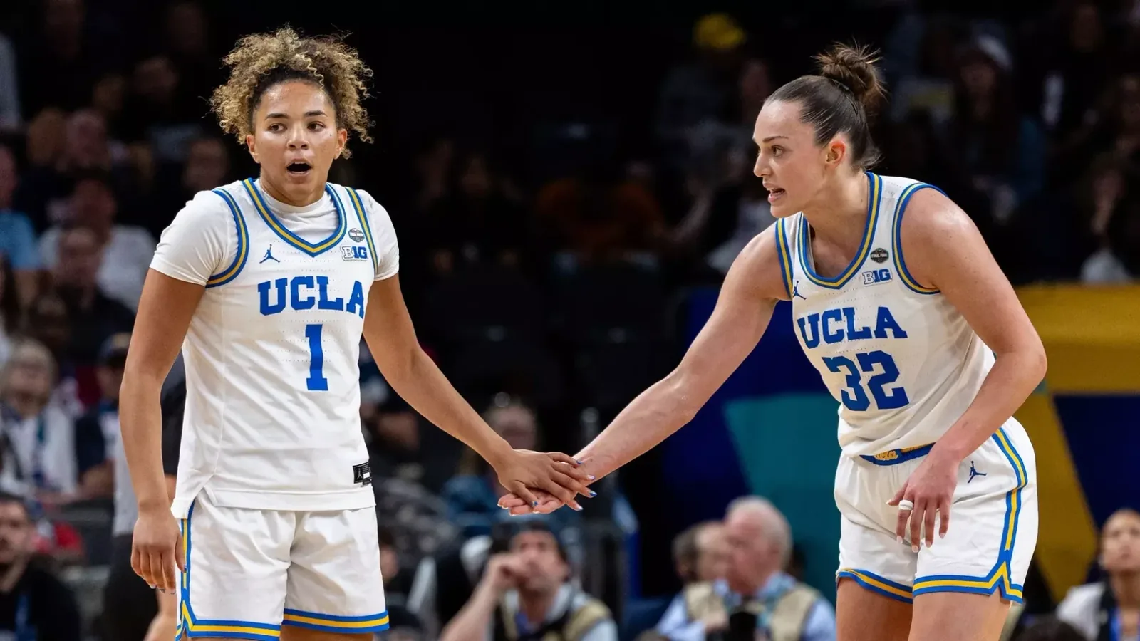 Two UCLA women's basketball players hold hands on the court